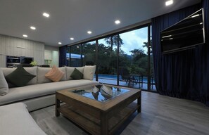 A modern living room with a sofa, coffee table, and large windows. - Sugar | Kamala Beach | 4-bedroom Pool Villa (Kamala)