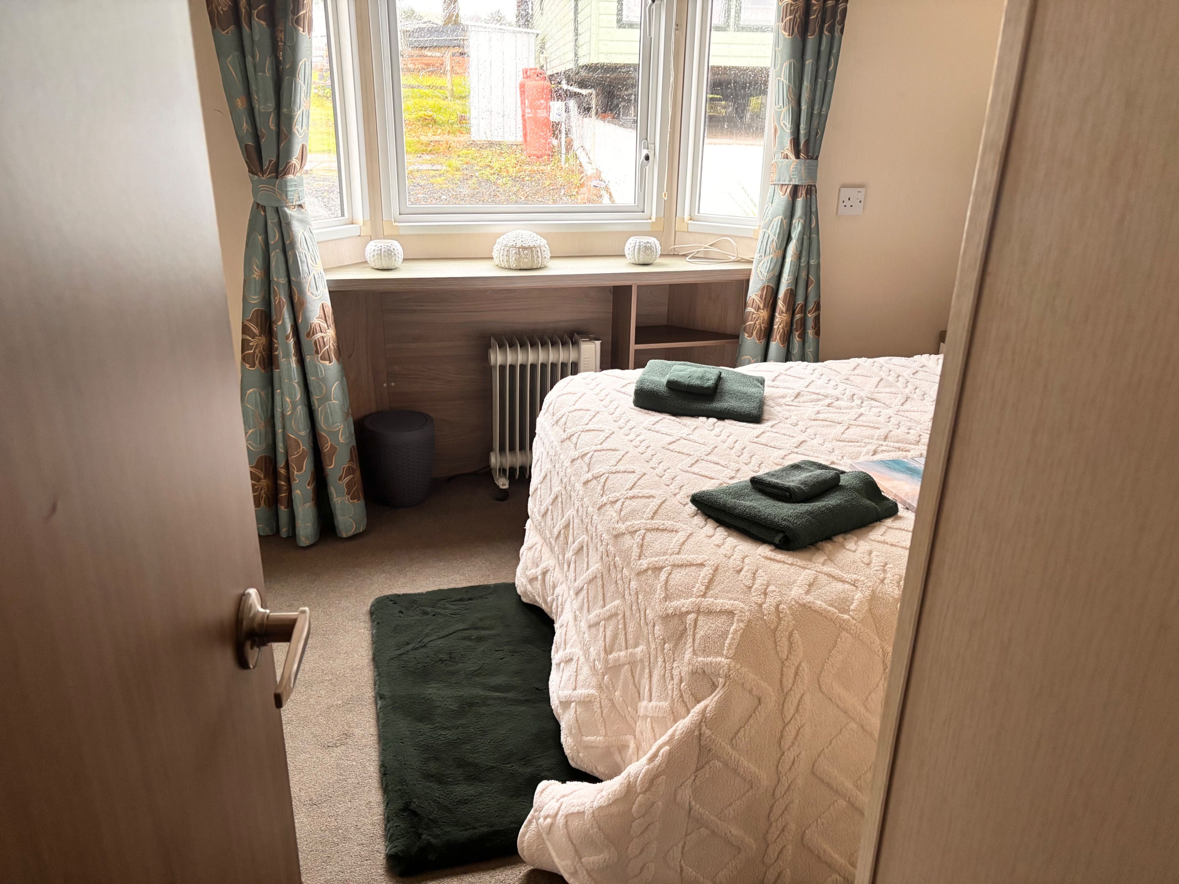 Een slaapkamer met een bed, een radiator, een raam met gordijnen en een deur.