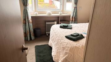 Een slaapkamer met een bed, een radiator, een raam met gordijnen en een deur.