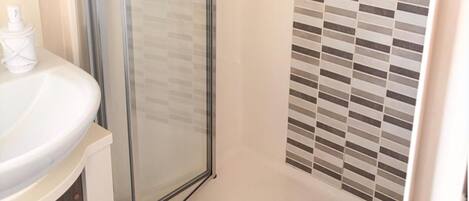 A bathroom with a glass shower enclosure, a white sink, and a tiled wall.