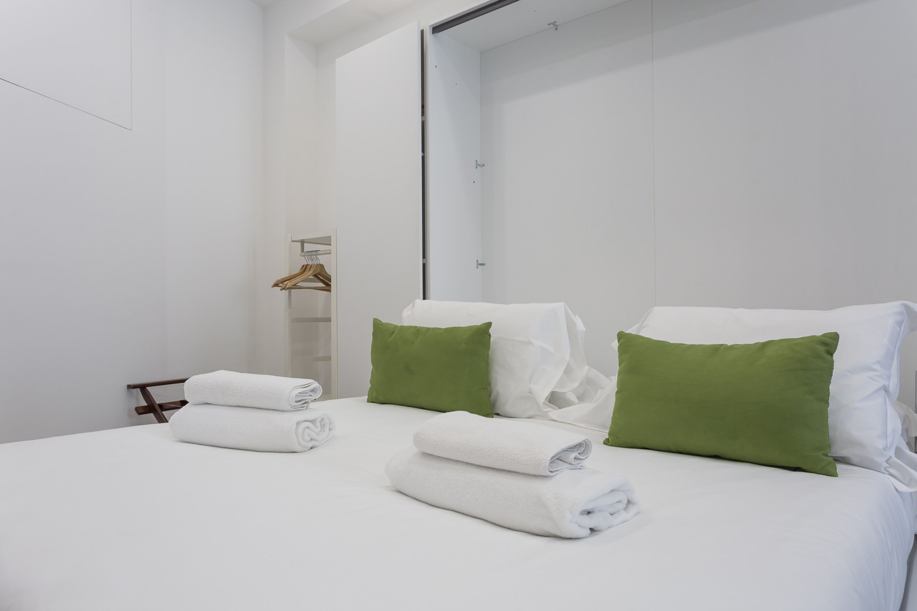 A hotel room with a bed, two green pillows, and two rolled towels.