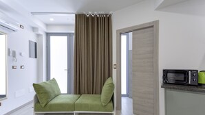 A modern living room with a sofa, a kitchen area with a microwave, and a door leading to another room. - Varenna Garden by Wonderful Italy (Perledo)