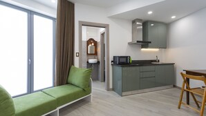 A modern living room with a green sofa, a wooden dining table, a kitchen area with a microwave, and a large window. - Varenna Garden by Wonderful Italy (Perledo)