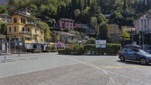 A cobblestone street with buildings, a parked car, and a hill with trees. - Varenna Garden by Wonderful Italy (Perledo)