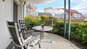A patio with a round table and two chairs, a white umbrella, and a potted plant. - Home port apartment 1 (Scharbeutz)