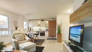 A modern living room with a sofa, ottoman, coffee table, and a flat-screen TV. - Home port apartment 1 (Scharbeutz)