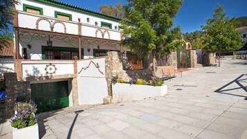 Un patio con un edificio de paredes de piedra, piso de baldosas y techo con tejas verdes.