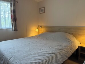 A bedroom with a bed, a bedside lamp, a window with curtains, and a framed picture on the wall. - Chalet auf Campingplatz (Windeck)