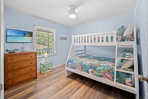 Une chambre avec un lit superposé, une commode, un téléviseur et une fenêtre avec des stores.