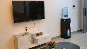 Een woonkamer met een flatscreen televisie, een waterdispenser, een koffiezetapparaat, een bank en een salontafel.
