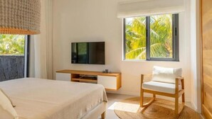 Ein Schlafzimmer mit Bett, Fernseher, Sessel und Fenster mit Blick auf Palmen.