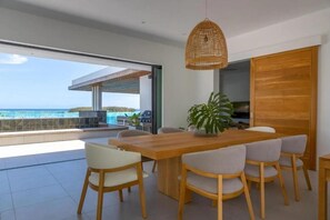 A modern dining area with a wooden table and chairs, a hanging light fixture, and a view of the ocean. - Blue Bay Luxury Penthouse offers stunning seaview and direct beachfront access. (Blue Bay)
