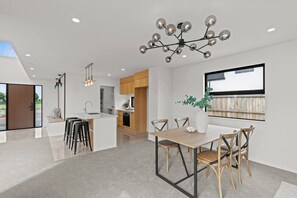 A modern kitchen with wooden cabinets, a dining area with a wooden table and chairs, and a unique chandelier.
