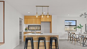 Una cocina moderna con una isla central, taburetes de bar, armarios de madera e iluminación colgante.