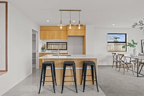 A modern kitchen with a central island, bar stools, wooden cabinetry, and pendant lighting.