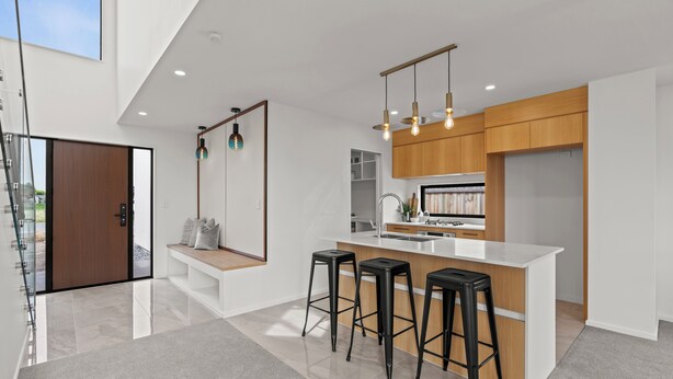 Una cocina moderna con una isla central, taburetes de bar, iluminación colgante y armarios de madera.