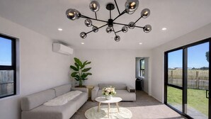 Una sala de estar moderna con un sofá gris, una mesa de centro redonda blanca, una planta en maceta y una lámpara de techo original.
