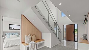 Un interior moderno con una escalera, una cama con cabecera de madera y un banco.