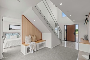 A modern interior with a staircase, a bed with a wooden headboard, and a bench.