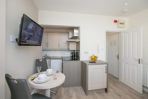 A compact kitchen with a dining area, a television mounted on the wall, and a small fruit bowl on the counter. - Portobello Court Apartments (Dublin)