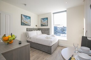 Una camera d'albergo moderna con un letto, un tavolo da pranzo con piatti e posate, una ciotola di frutta e due quadri alle pareti.