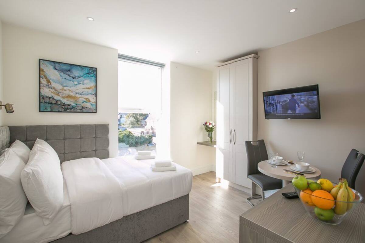 A modern hotel room with a bed, a dining area, a TV, and a balcony with a view.