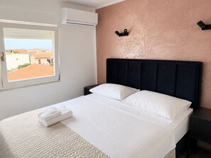 A hotel room with a bed, a nightstand, an air conditioning unit, and a window with a view of buildings. - Mediterraneo room S1 (Sukošan)