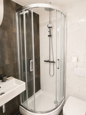 Ein modernes Badezimmer mit einer gläsernen Duschkabine, einem weißen Waschbecken und einer Toilette.
