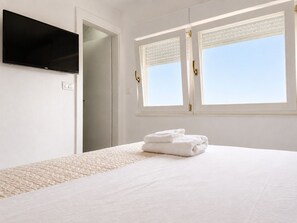 Ein Hotelzimmer mit einem Bett, einem Flachbildfernseher, einem Fenster mit Jalousien und einer Tür.