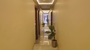 A hotel hallway with a polished floor, potted plants, and a door at the end. - HOTEL BELVA (Ahmedabad)