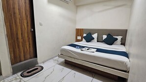 A bedroom with a bed, a wooden door, a small plant, and a tiled floor. - HOTEL BELVA (Ahmedabad)