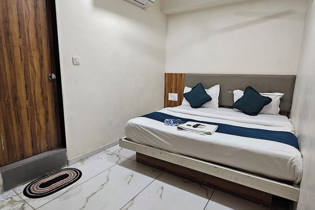 A bedroom with a bed, a wooden door, a small plant, and a tiled floor.