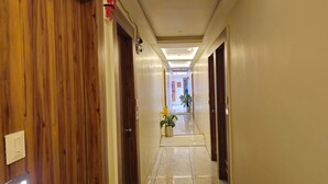 A hotel hallway with wooden doors, a potted plant, and a tiled floor. - HOTEL BELVA (Ahmedabad)