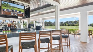 Een overdekt terras met een bar, een televisie, barstoelen en uitzicht op een golfbaan.