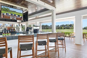 A covered outdoor bar area with a television, bar stools, and a view of a golf course.