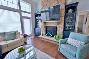 A living room with a fireplace, a sofa, a coffee table with a plant, and a bookshelf.