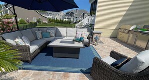 A patio with a sectional sofa, a coffee table, wicker chairs, a blue rug, and a barbecue grill.