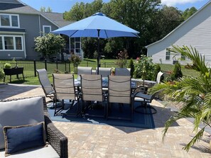 Een terras met een tafel en stoelen, een blauwe parasol en een stenen vloer.