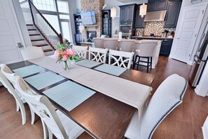 A dining area with a long table, white chairs, and a vase of flowers.