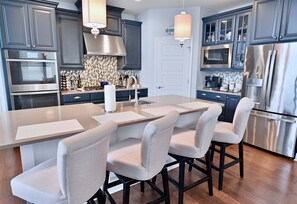 A modern kitchen with dark cabinets, stainless steel appliances, a central island with bar stools, and pendant lighting.