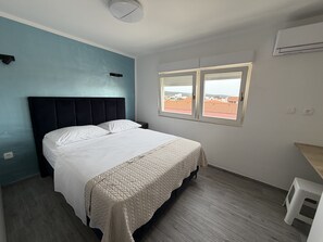 Ein Schlafzimmer mit Bett, Fenster, Hocker und Klimaanlage.