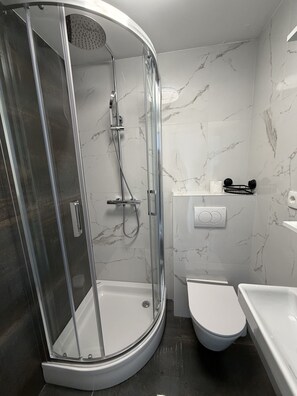 Ein modernes Badezimmer mit einer gläsernen Duschkabine, einer weißen Toilette und einer Badewanne.