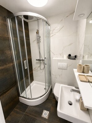Ein modernes Badezimmer mit einer gläsernen Duschkabine, einem weißen Waschbecken und einer Toilette.