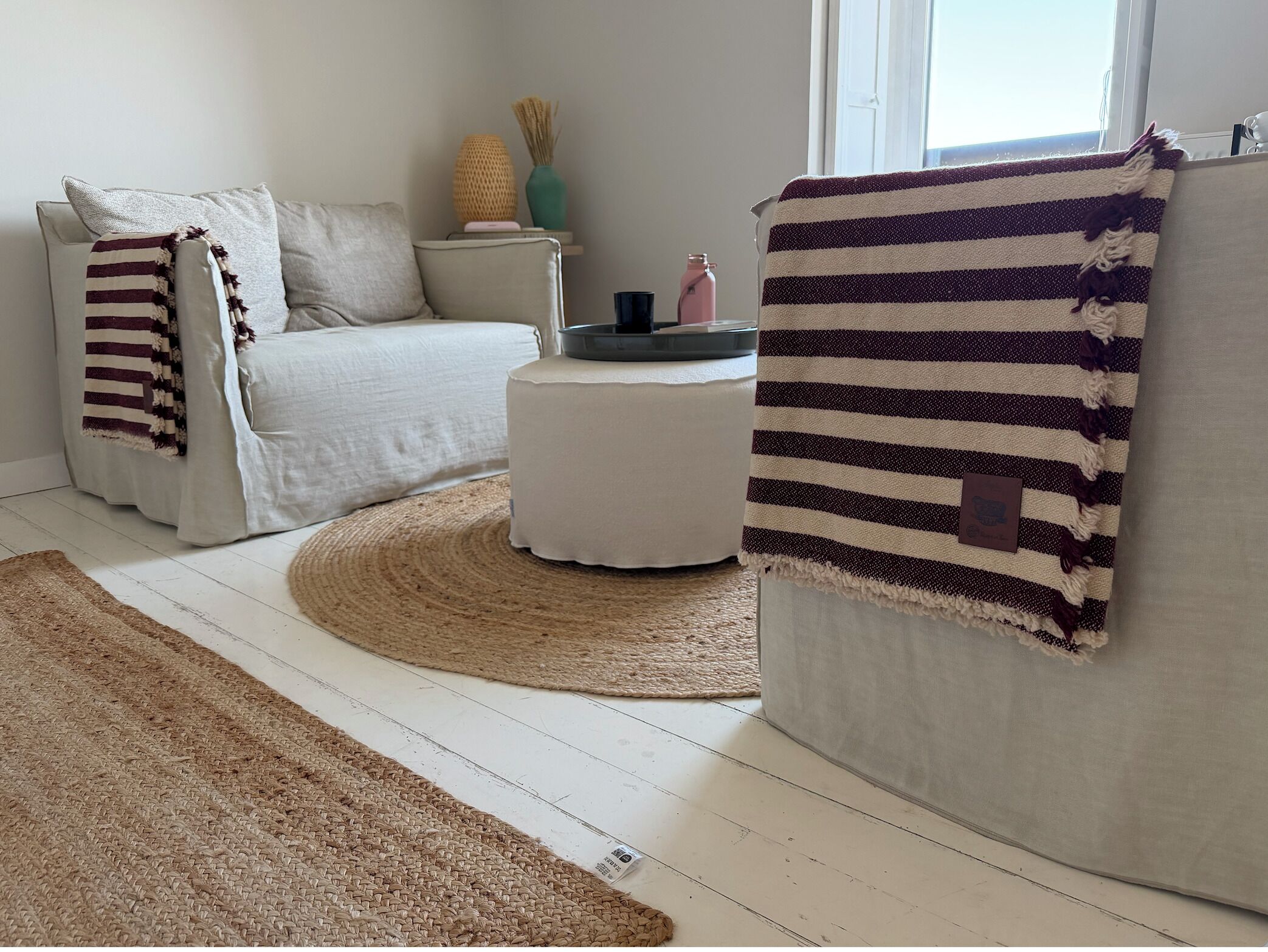 A living room with a sofa, ottoman, and striped throw.