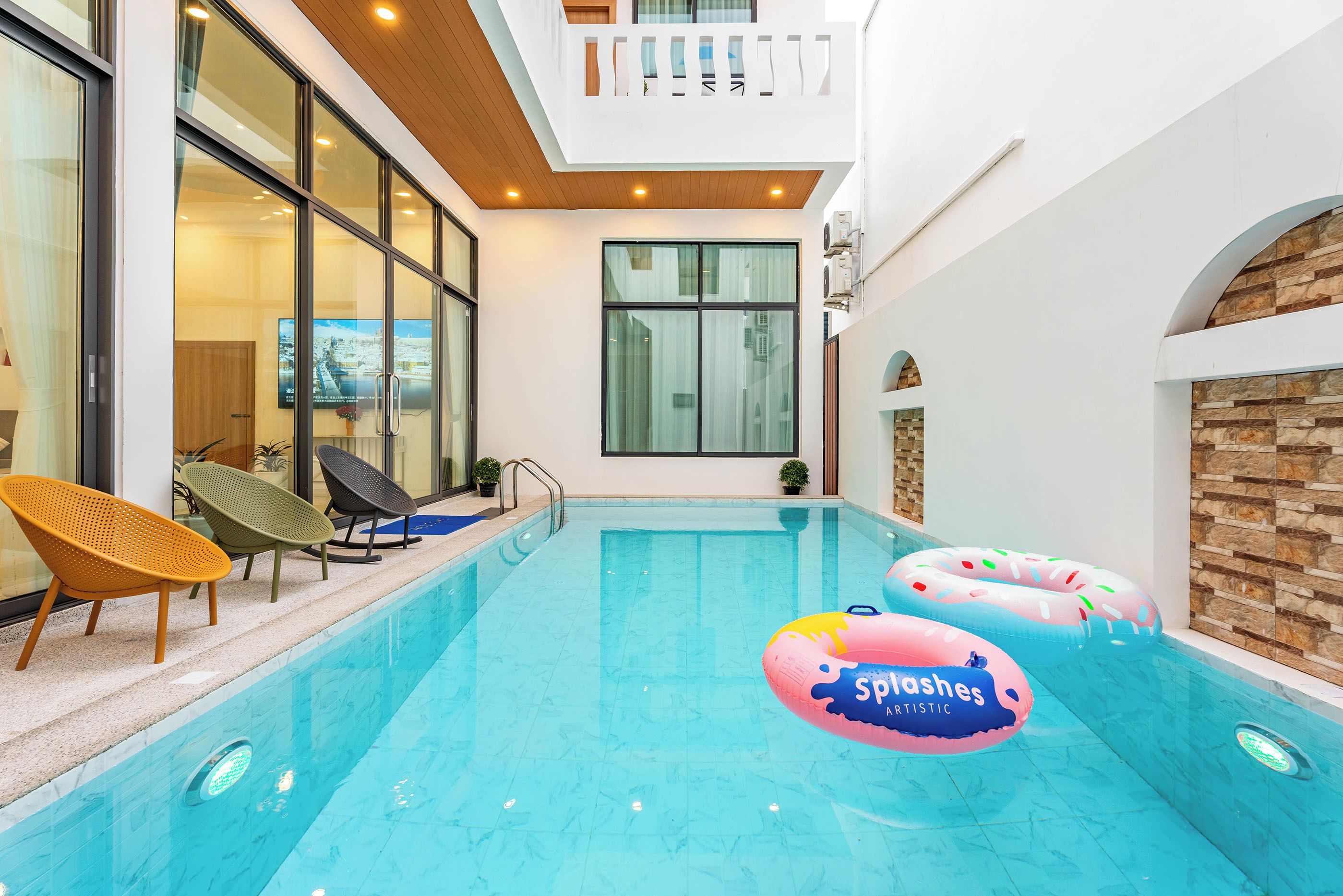An indoor swimming pool with clear water, surrounded by lounge chairs and a view of a cityscape through large windows.