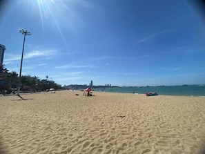 Una playa arenosa con cielo despejado, un poste de luz alto y un horizonte urbano distante.