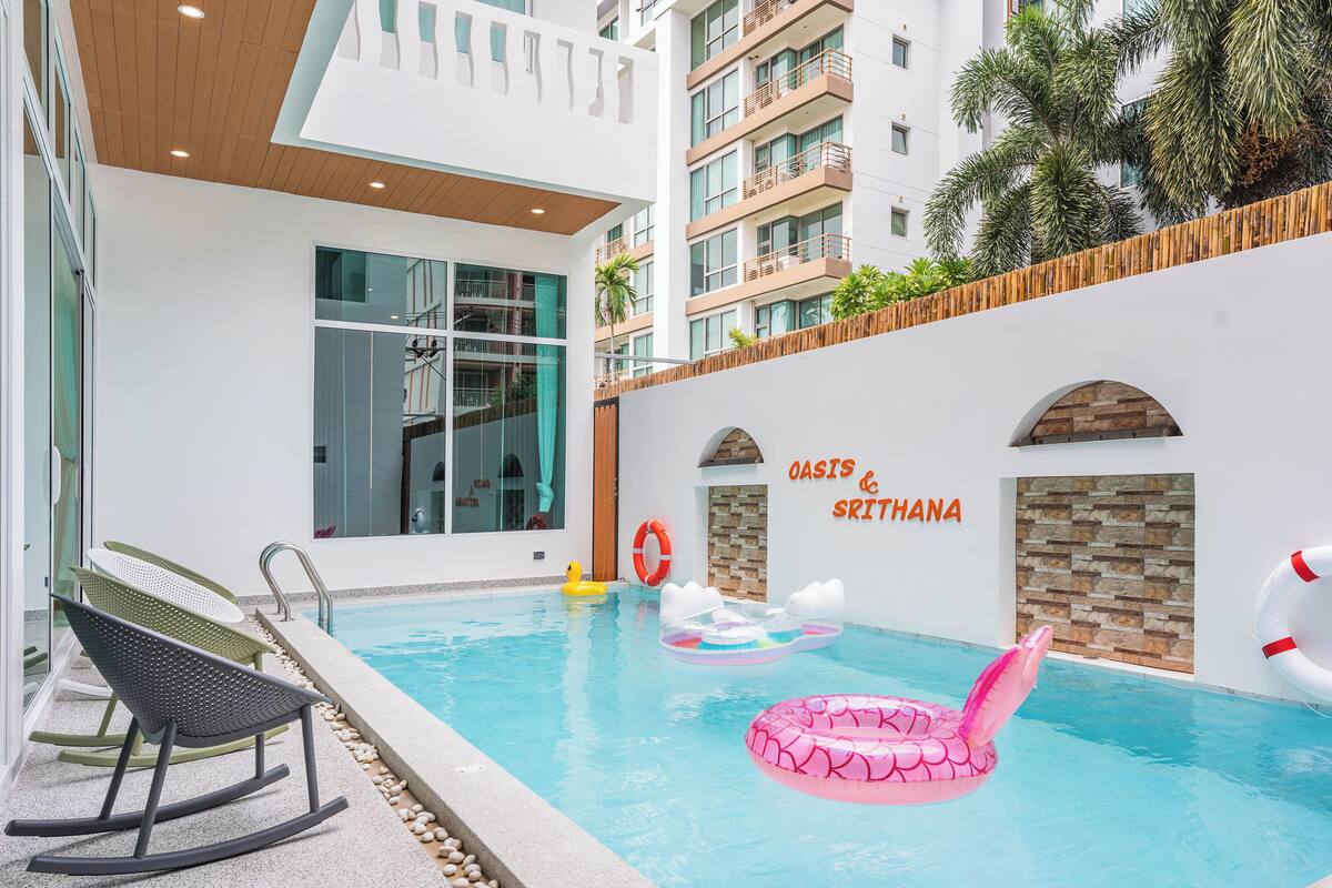 A swimming pool with inflatable toys, a rock chair, and a wall with the text 'OASIS & SRI THANA'.