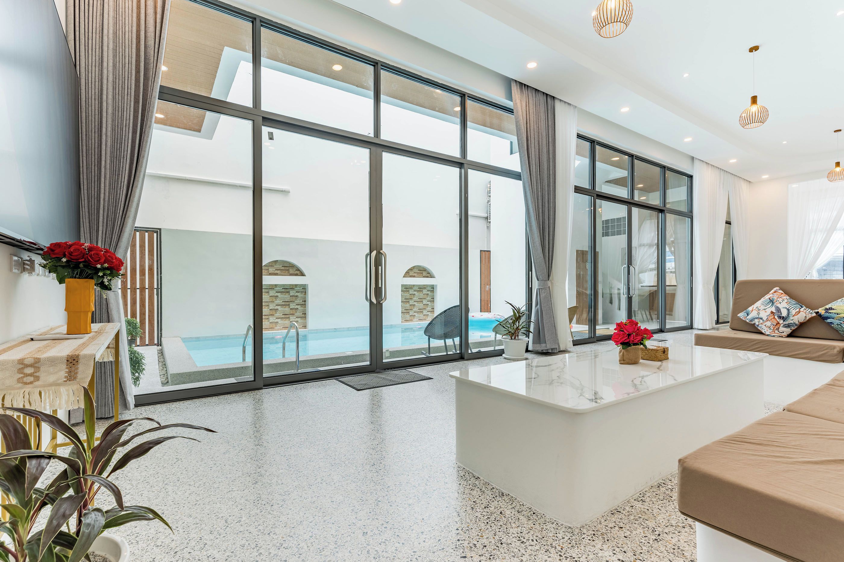 A modern living room with a large glass door leading to a pool area, a marble countertop, and a beige sofa.