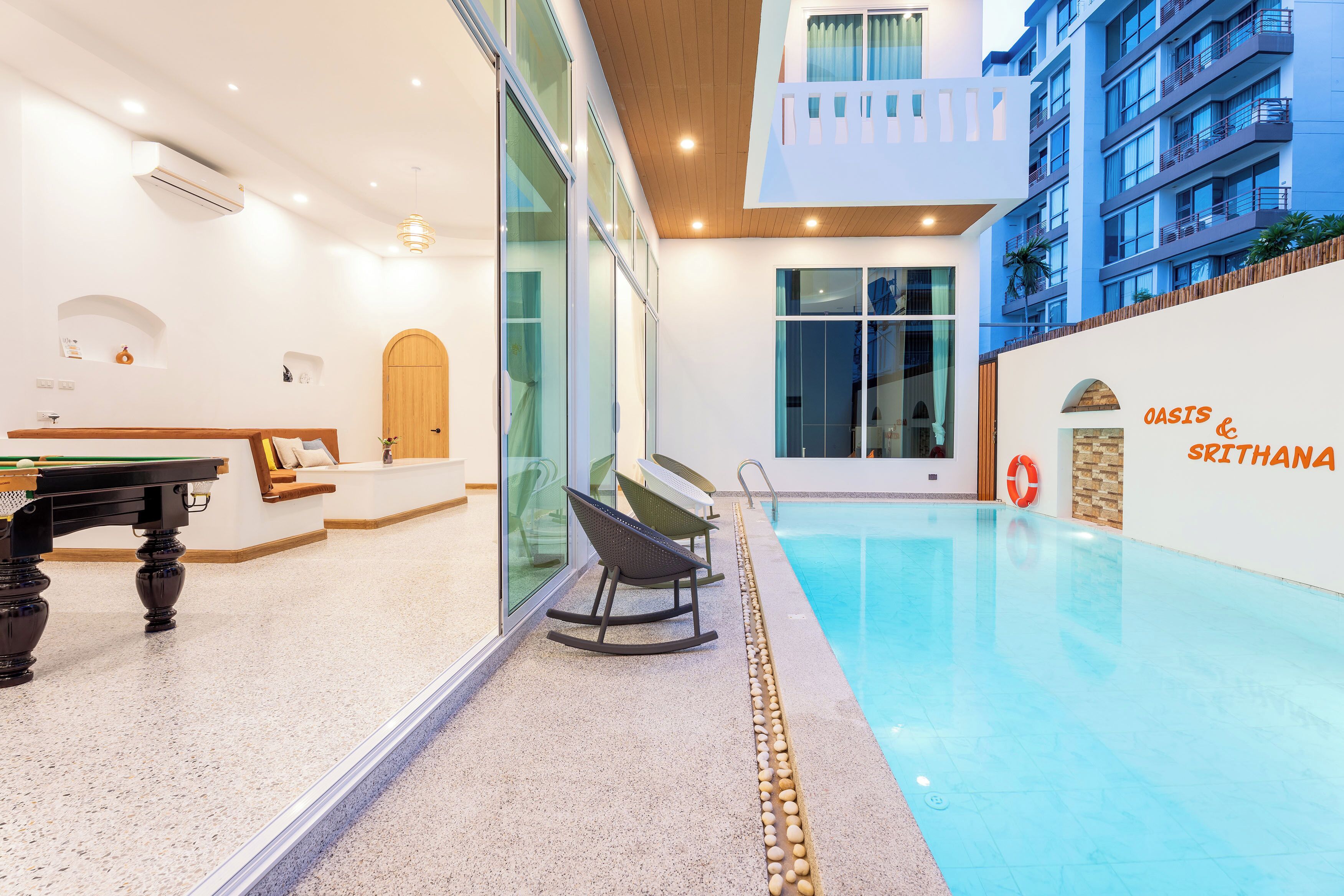 A modern indoor pool area with a pool table, seating, and a view of the building's exterior.