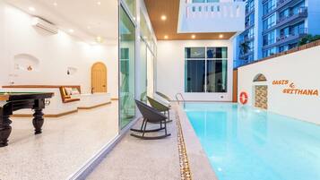 A modern indoor pool area with a pool table, seating, and a view of the building's exterior.